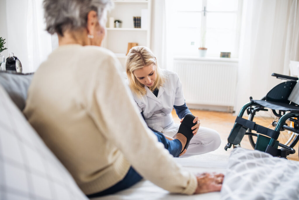 a health visitor putting on slippers on a senior woman at home.